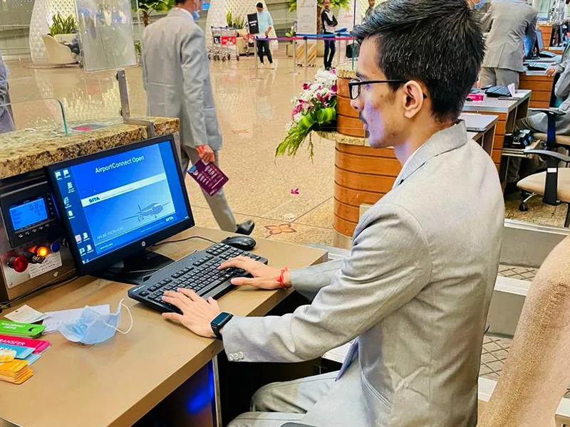 A check-in agent at an airline counter, working the departure screen with boarding passes on the desk
