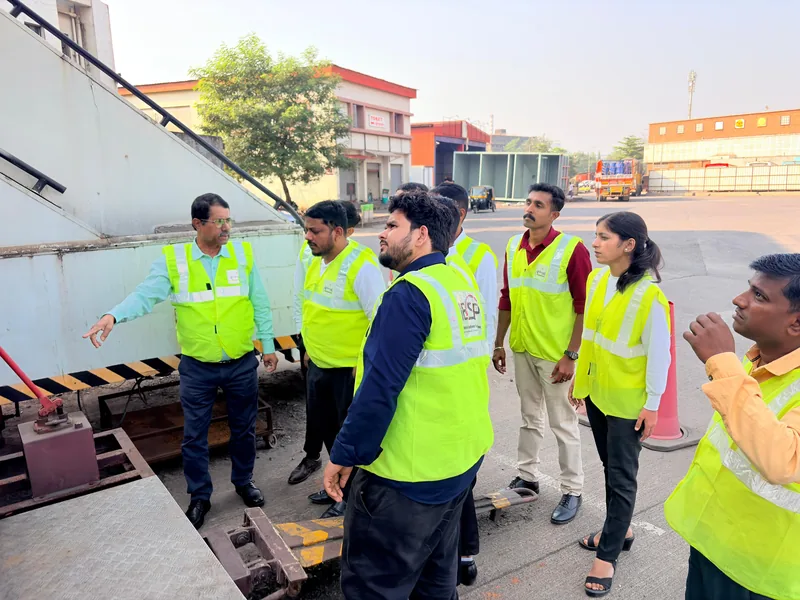 An instructor briefing students in high visibility vests beside a cargo pallet loader