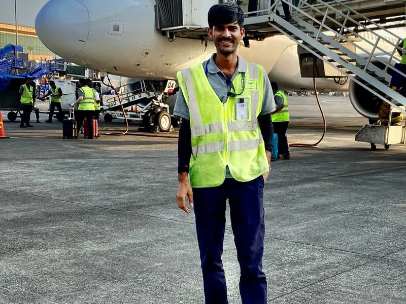 An IESP student in a high visibility vest on the apron beside an aircraft and a jet bridge
