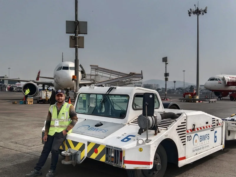 An IESP student in a high visibility vest beside an aircraft tug on the apron